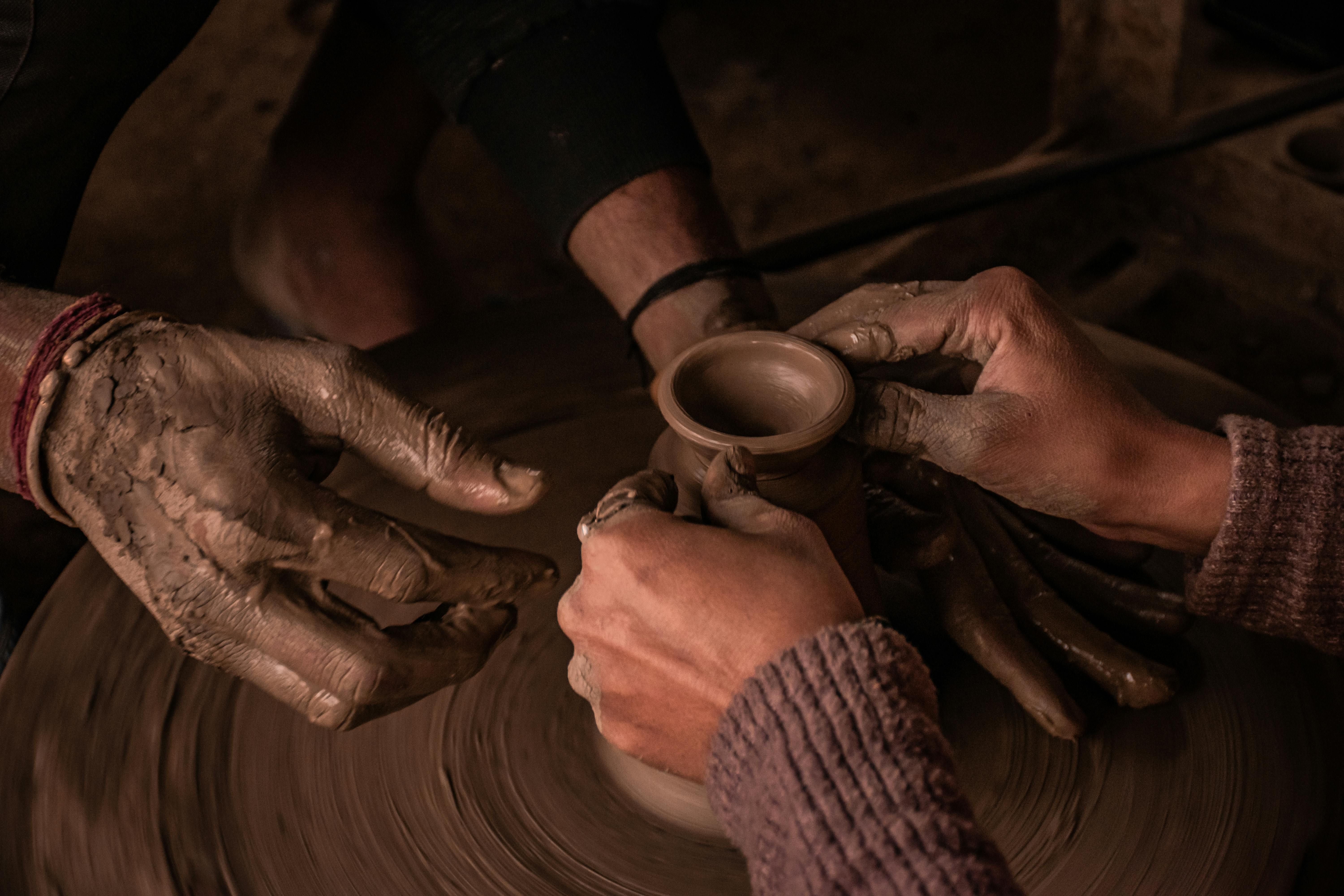 Several pairs of hands shaping clay together on a pottery wheel